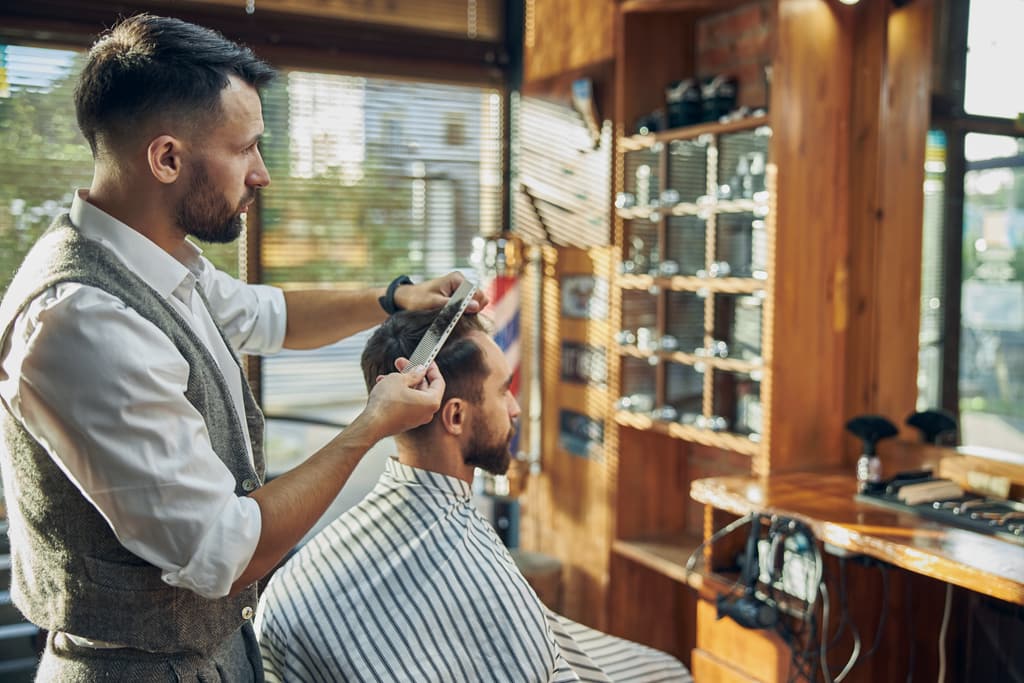 Barbero con chaleco cortando el pelo a un cliente en una barbería clásica de madera.